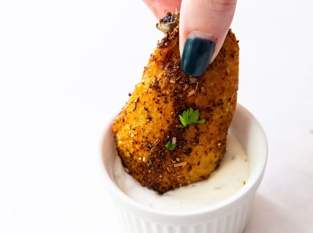 one chicken wing dunked into ranch with a hand holding it.