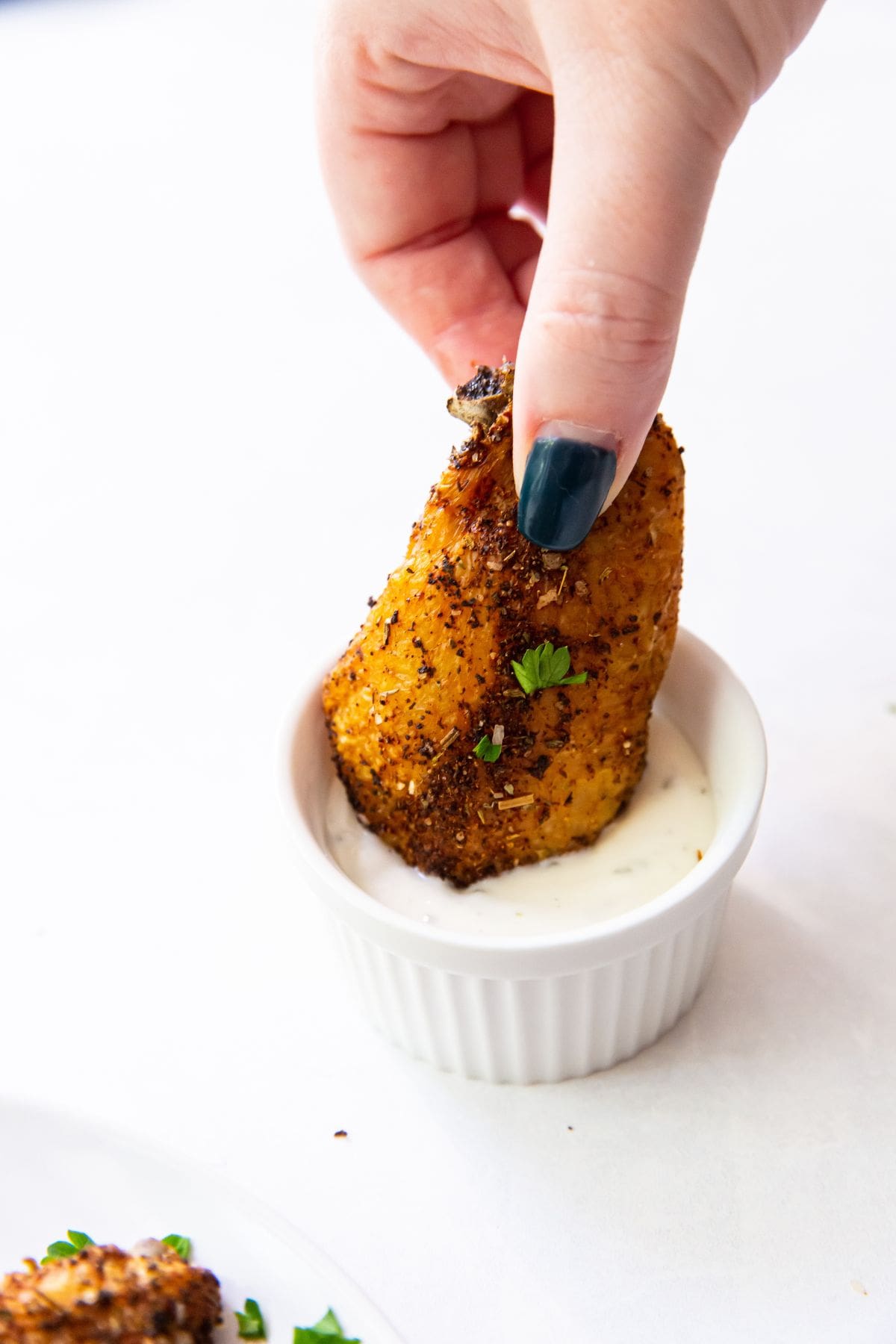 one chicken wing dunked into ranch with a hand holding it.