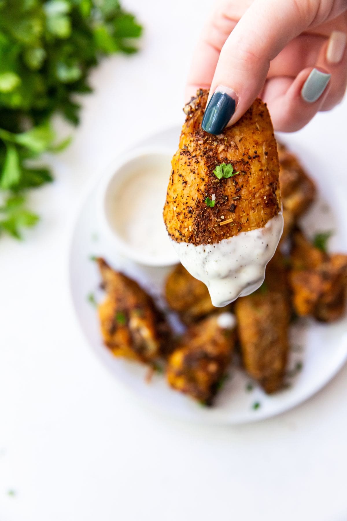 chicken wing with keto dry rub being held with parsley up close dipped in ranch dressing