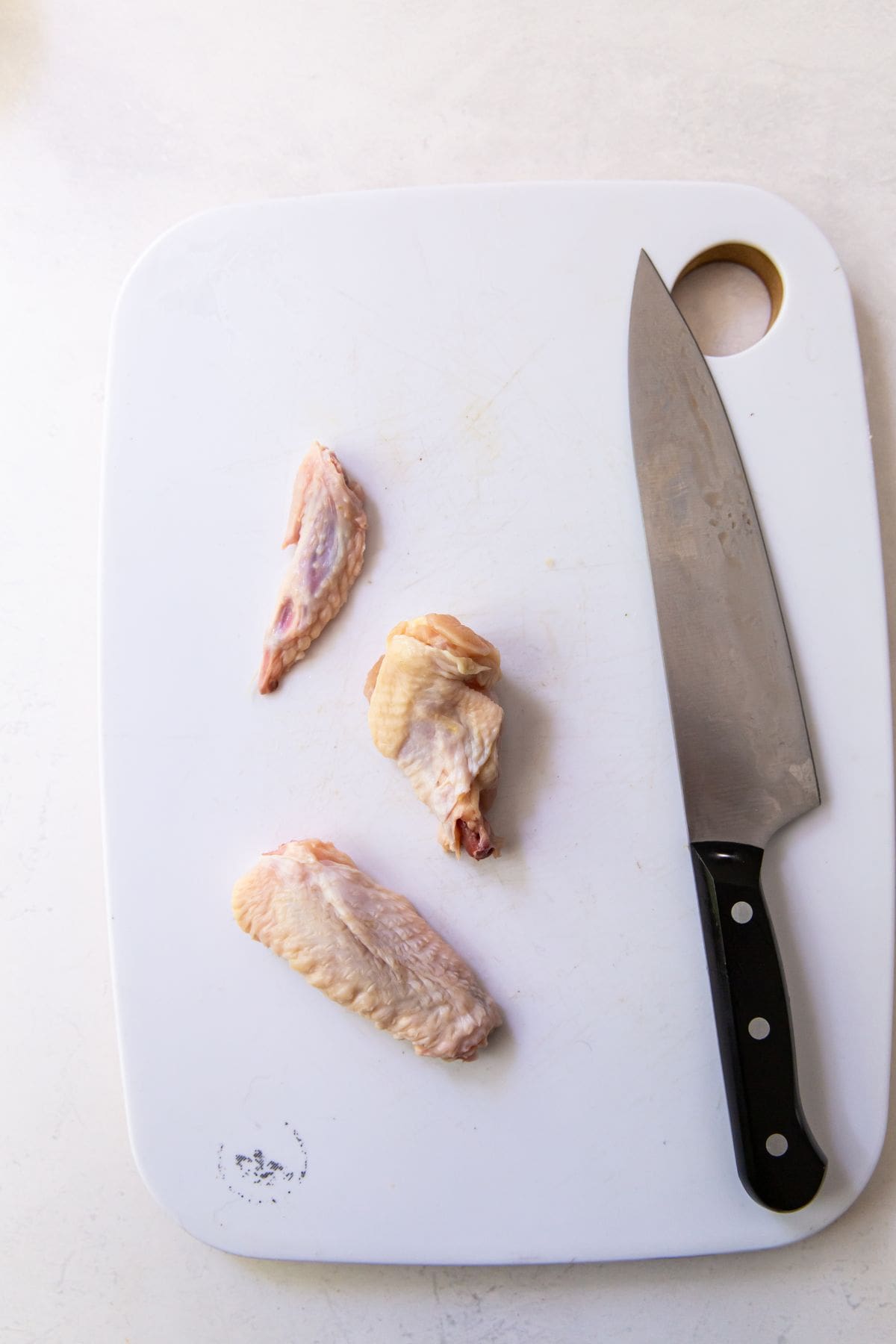 white cutting board with one chicken cut into wing and drum. knife on the side.