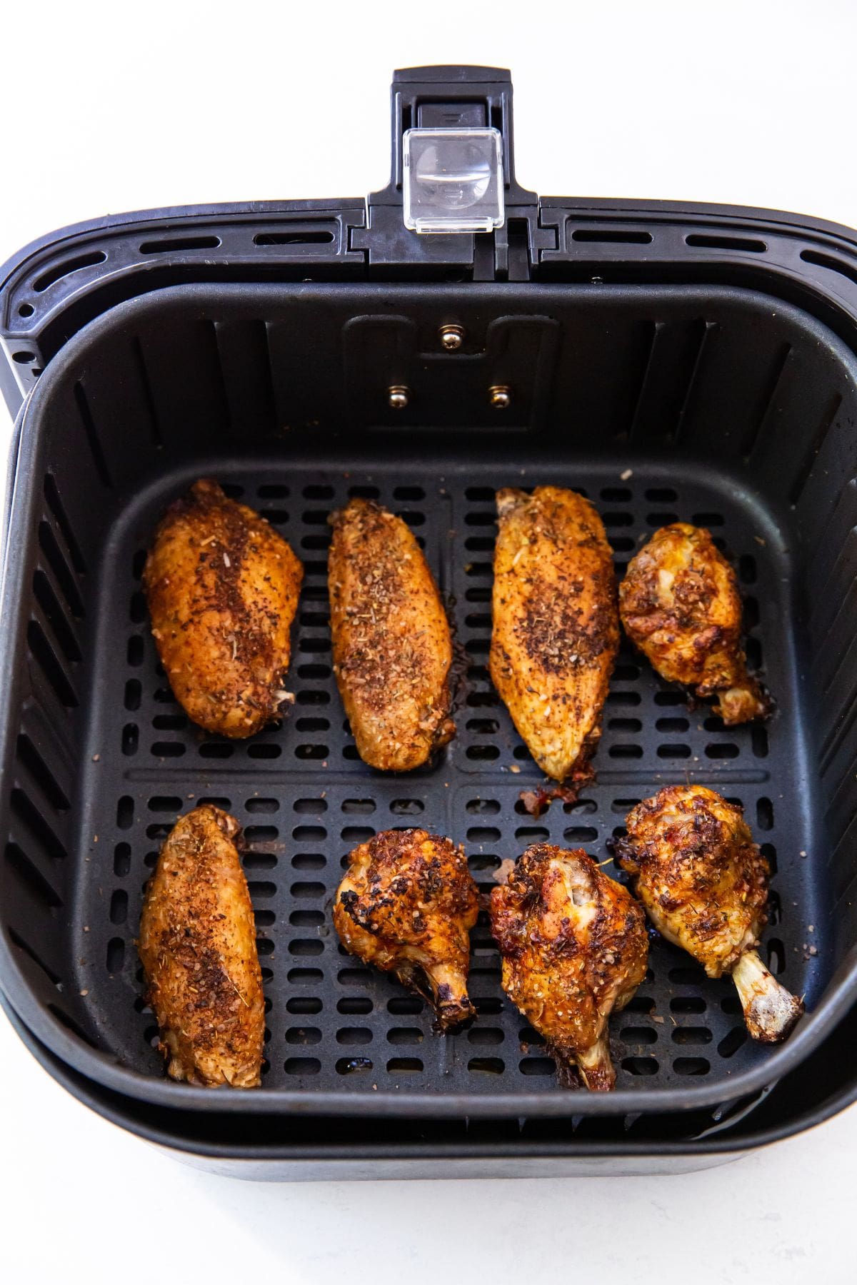 Black Air fryer with cooked chicken wings inside.