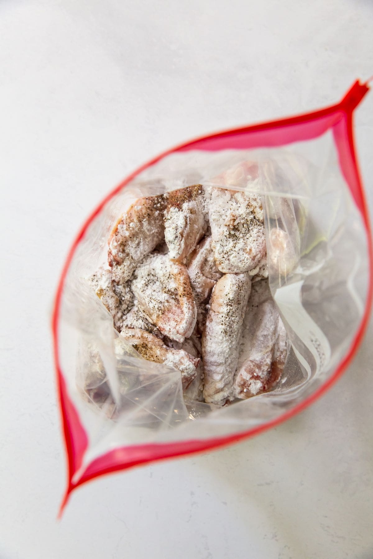 ziplock bag with raw chicken wings tossed in baking soda salt and black pepper