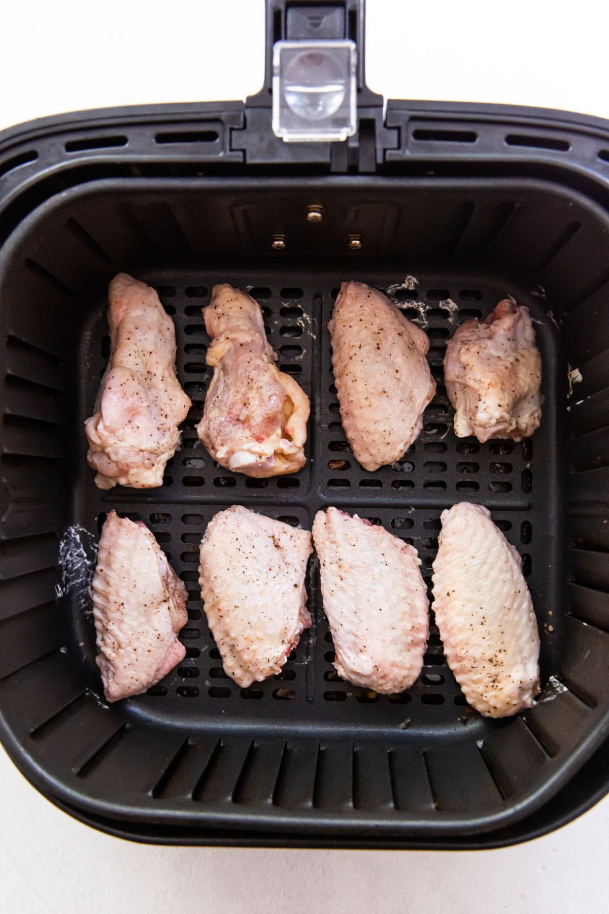 Black air fryer with raw chicken wings inside it 