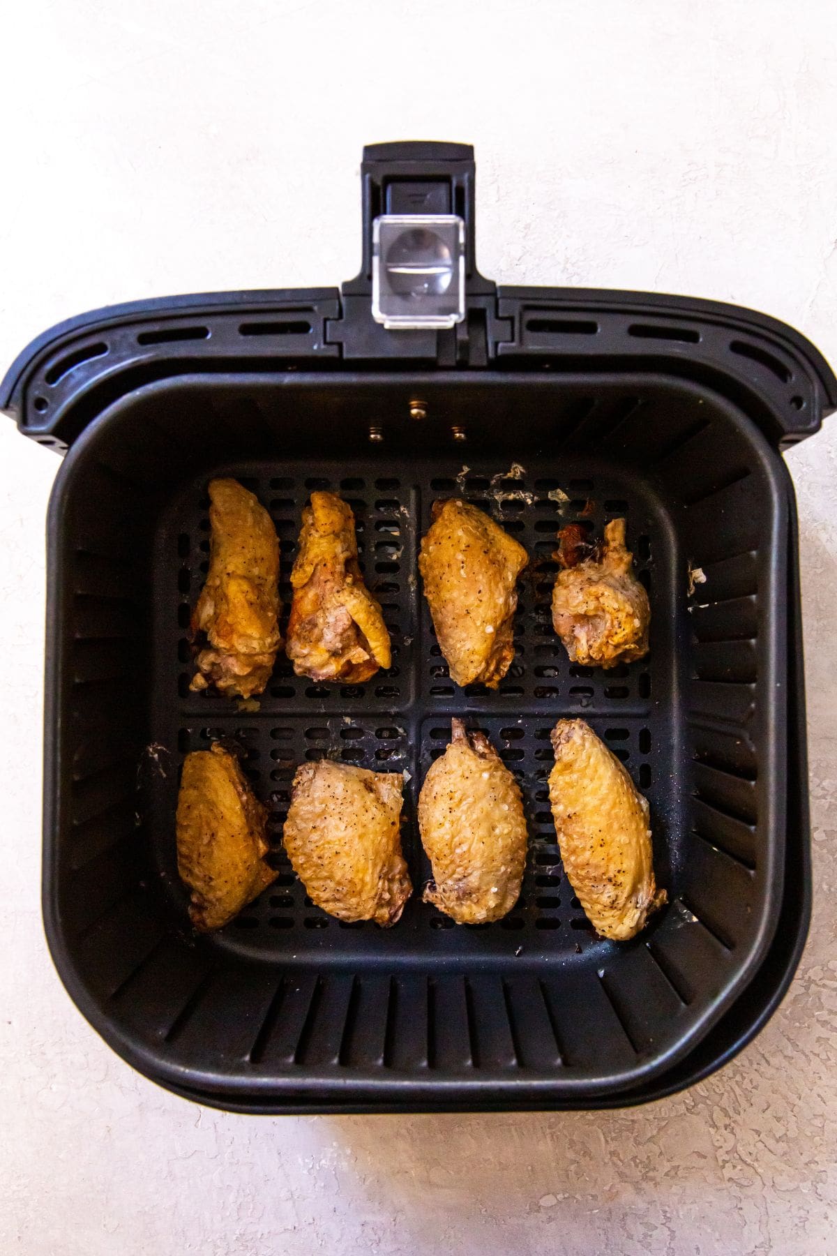 Black air fryer with cooked chicken wings inside