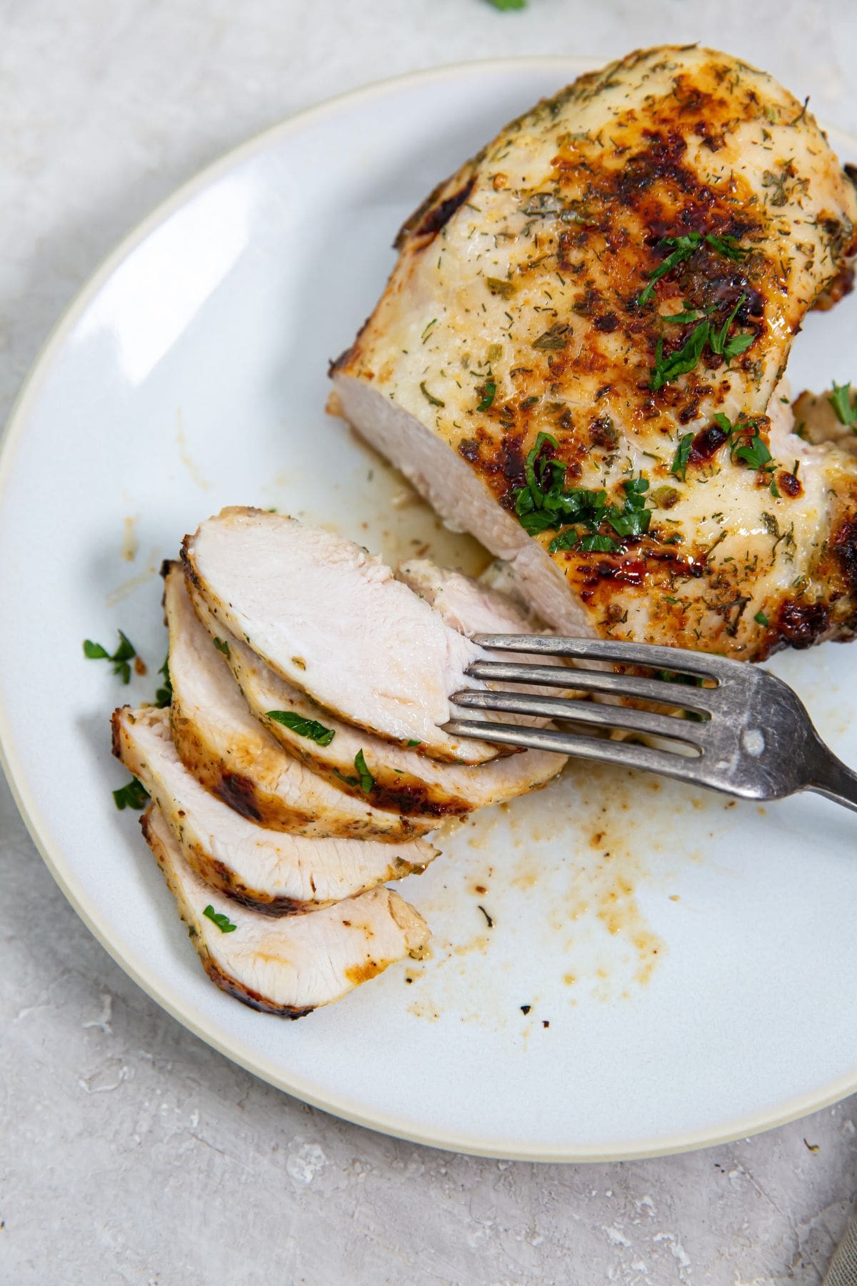 white plate with chicken breast on it parsley in the back. fork on the plate