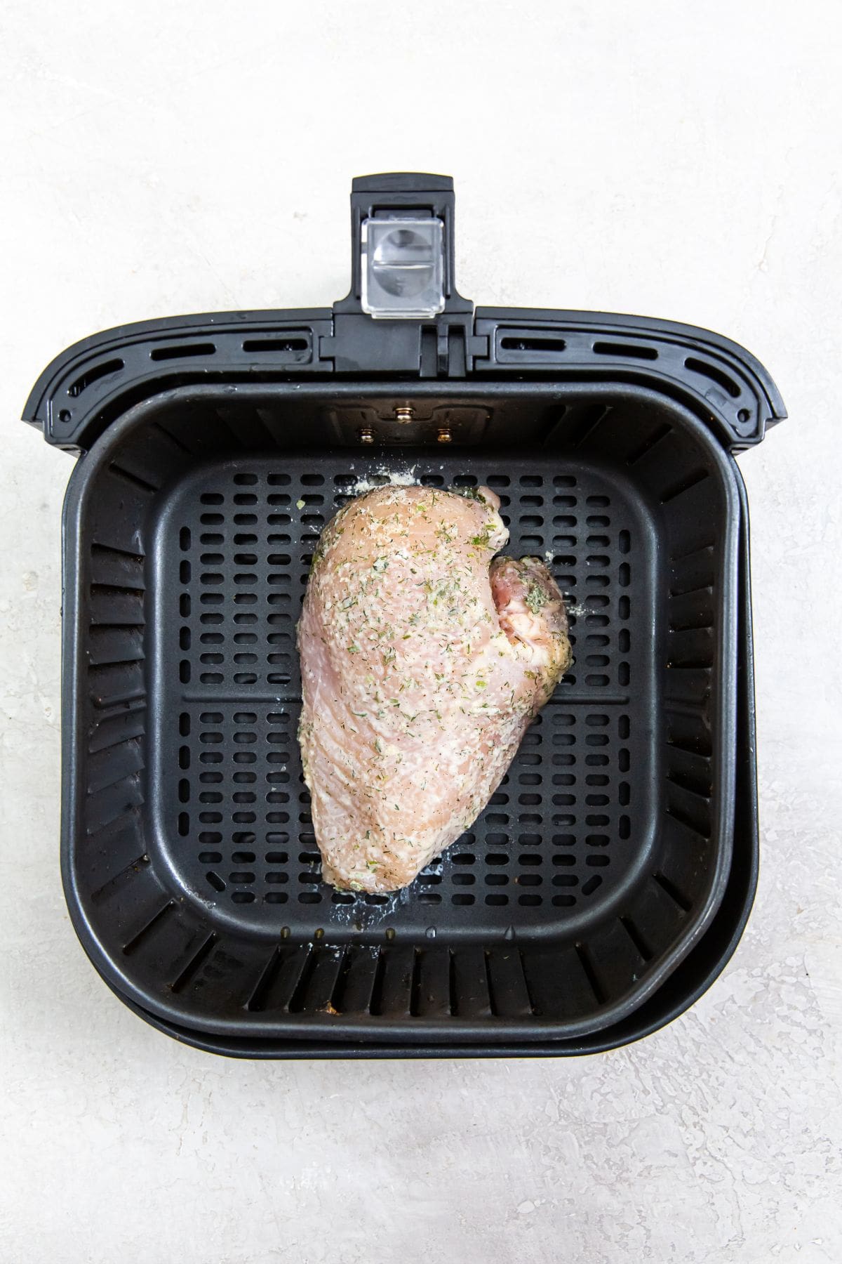 black air fryer with raw chicken inside