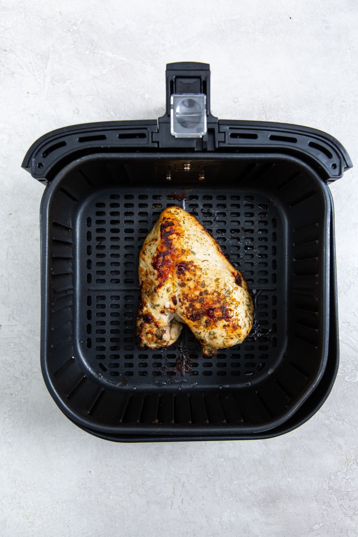 black air fryer with cooked chicken inside