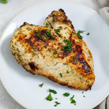 white plate with chicken breast on it parsley in the back green towel next to it