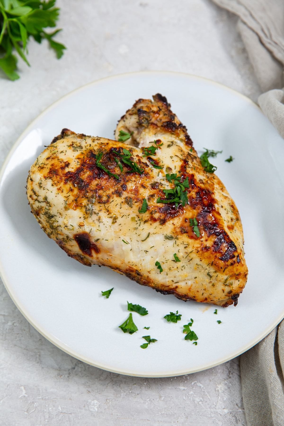 white plate with chicken breast on it parsley in the back green towel next to it