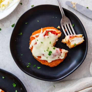 black plate with chicken patty parm a piece cut out and on a fork