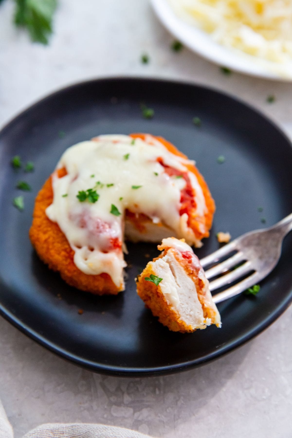 black plate with chicken patty parm a piece cut out and on a fork