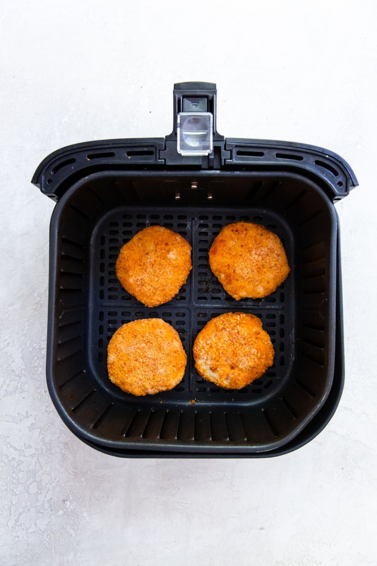 black air fryer with cooked chicken Patties inside