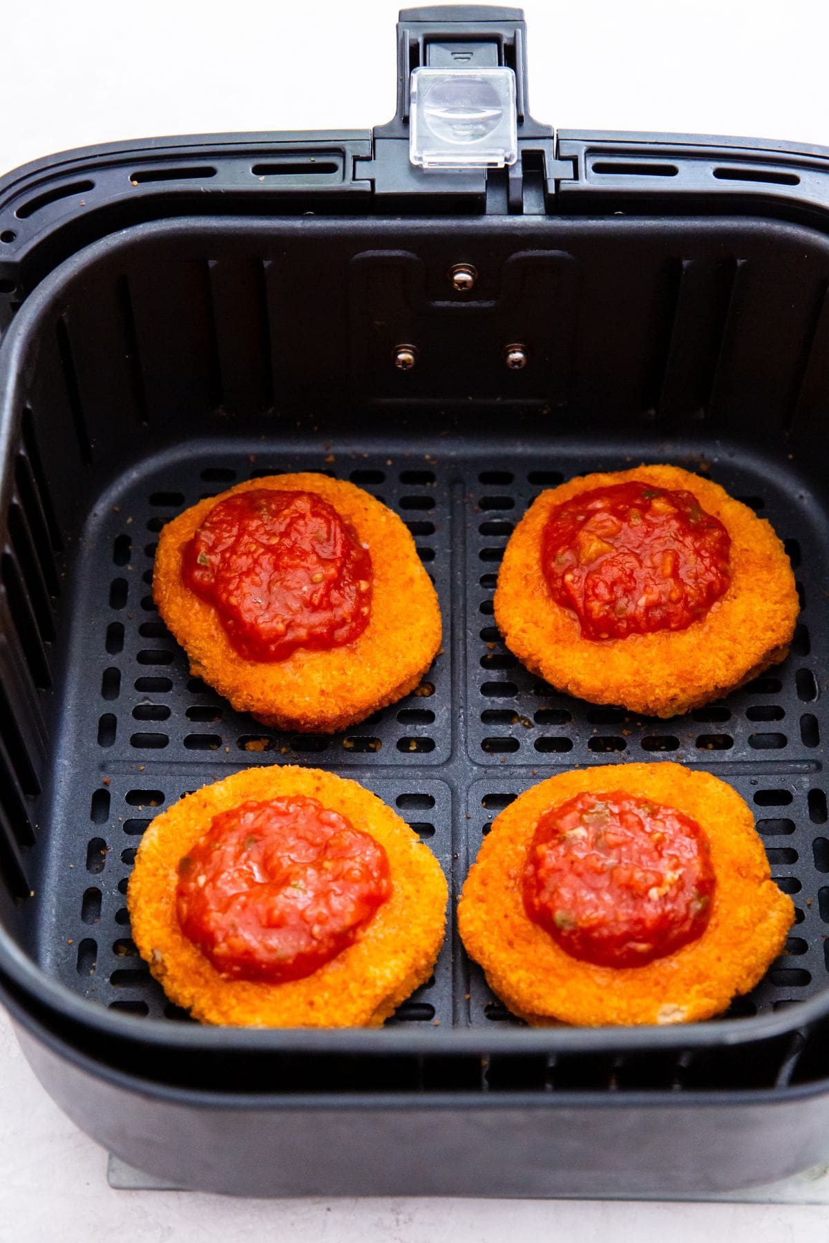 black air fryer with chicken patties inside topped with pizza sauce