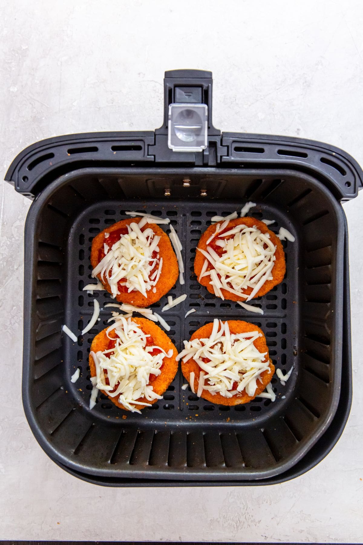 black air fryer with chicken patties inside pizza sauce and mozzarella on top