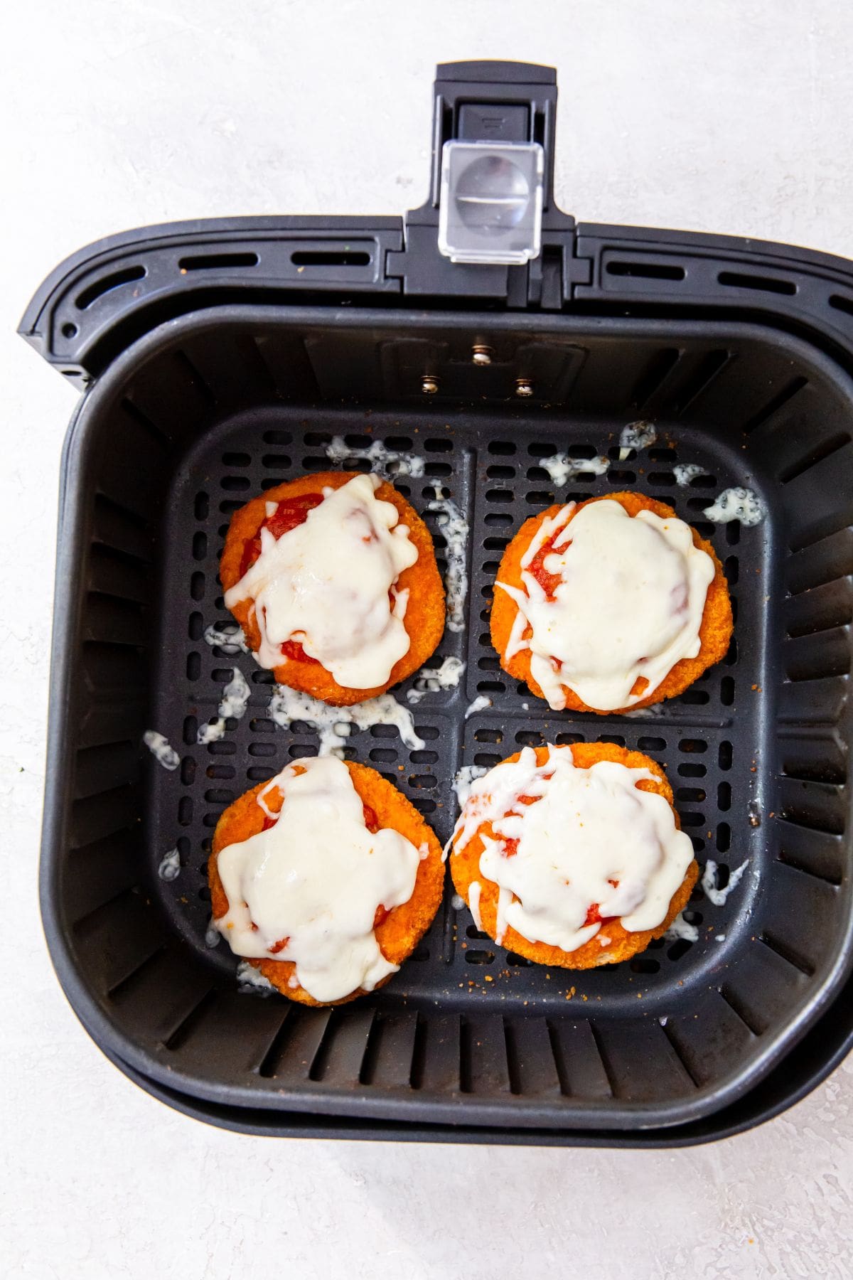 black air fryer with chicken patties inside topped with pizza sauce and melted mozzarella