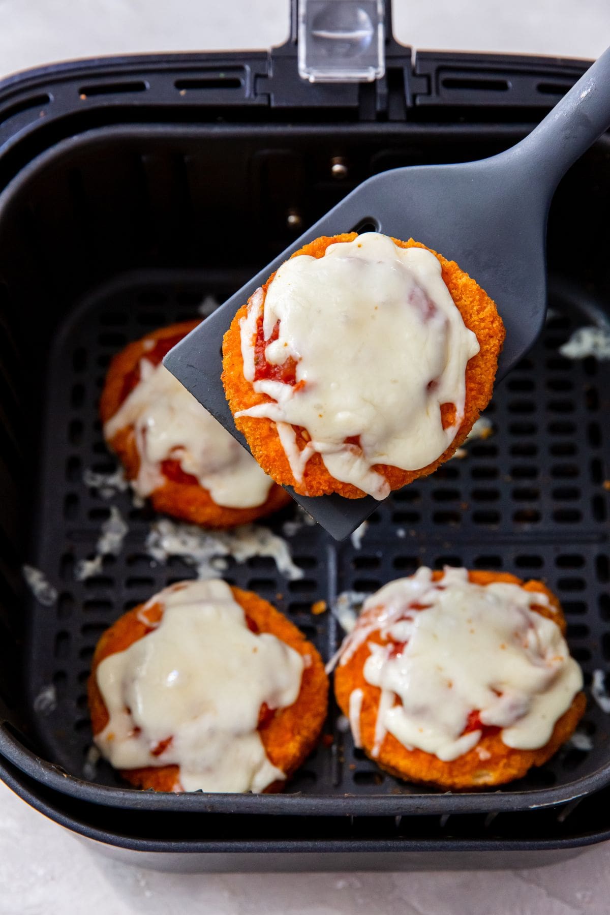 black air fryer with chicken patty with pizza sauce and melted cheese.