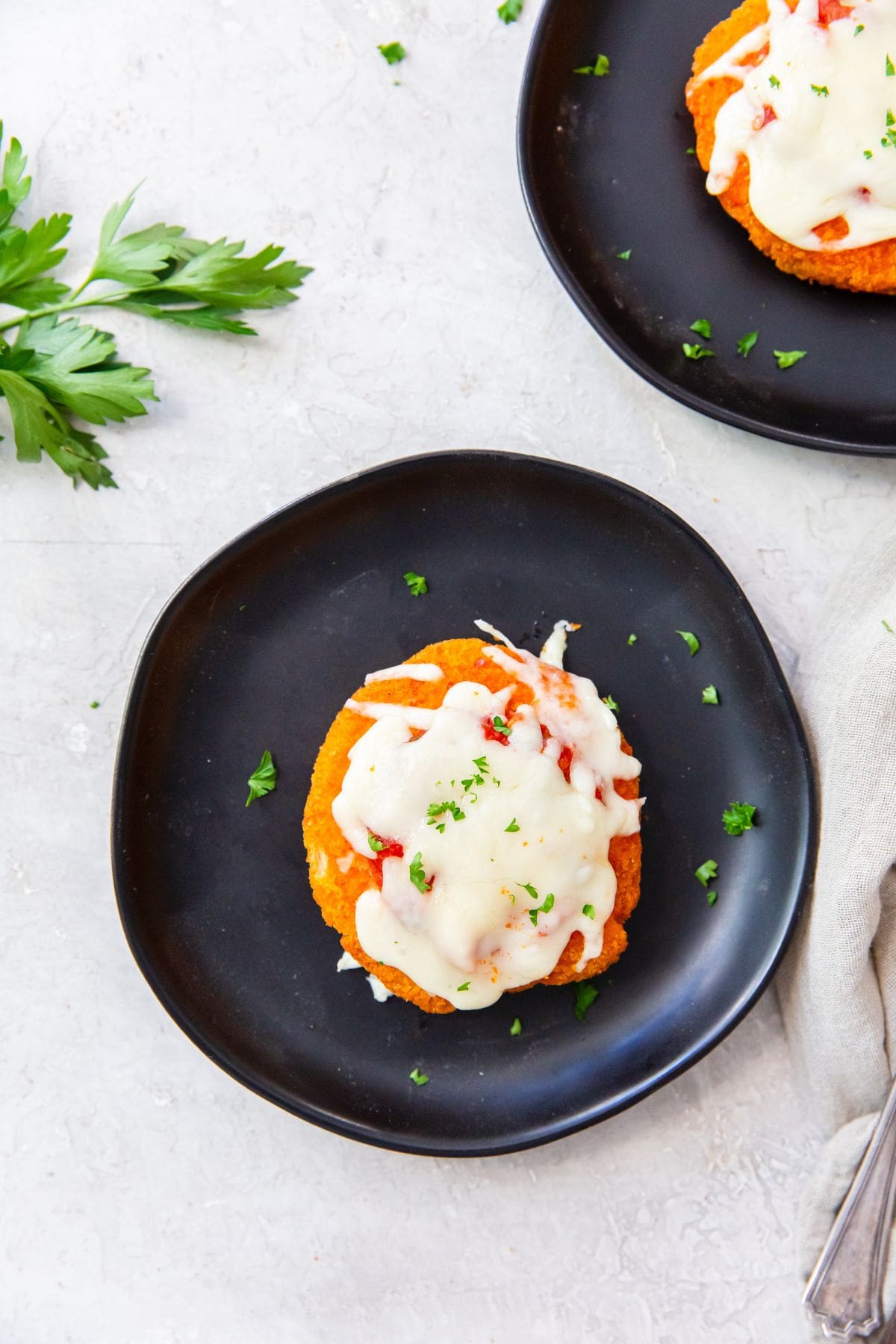 two black plates with chicken patty Parm on it parsley in the back