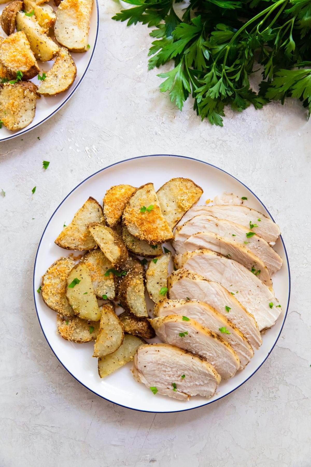 two plates with chicken breast and potatoes parsley in the back