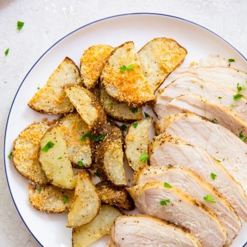 two plates with chicken breast and potatoes parsley in the background