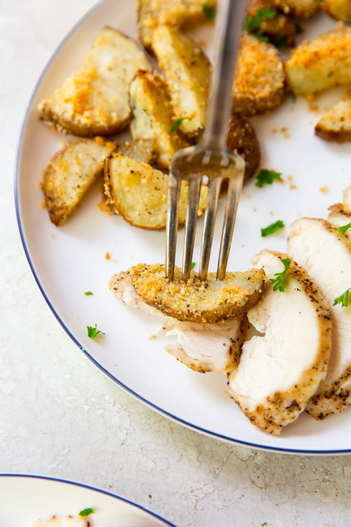 white plate with chicken and potatoes. a fork in a piece of chicken