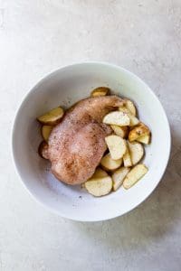 white bowl with seasoned chicken breast and potatoes inside.