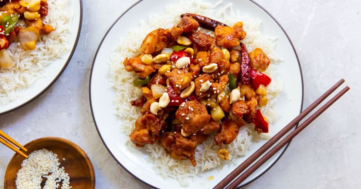 two plates of kung pao chicken chop sticks on one plate and a bowl sesame seeds next to it