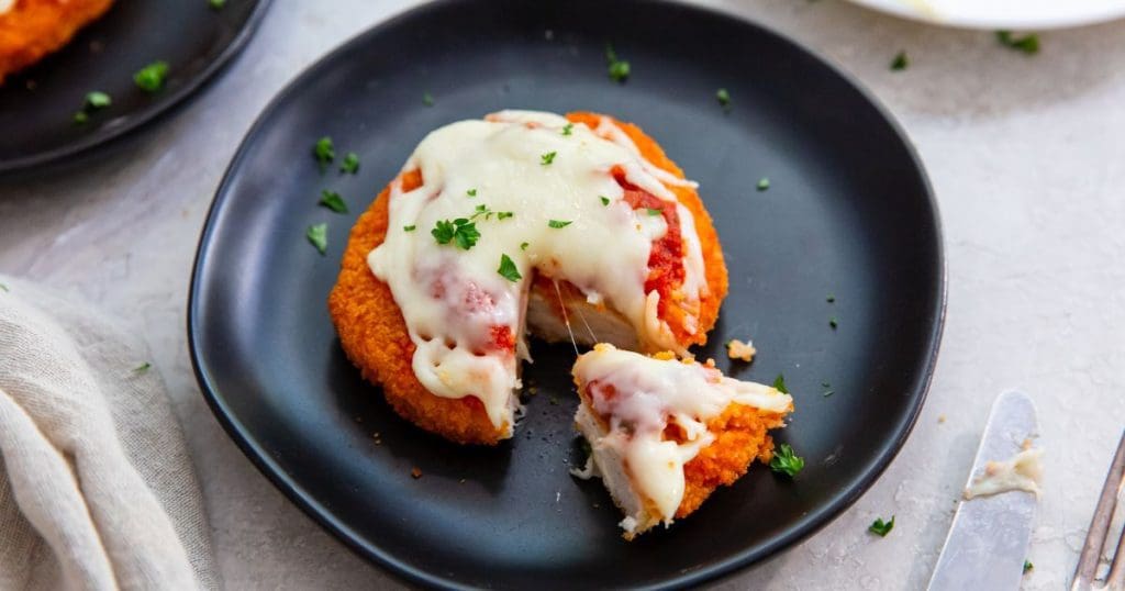 chicken patty parm with a piece cut out green towel next to plate with knife