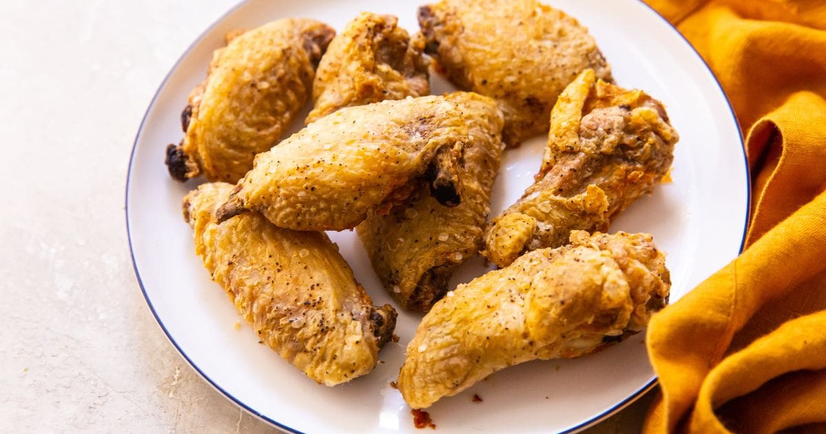 Crispy Air Fryer Chicken Wings with Baking Powder on a white plate with parsley and a white sauce on the side.