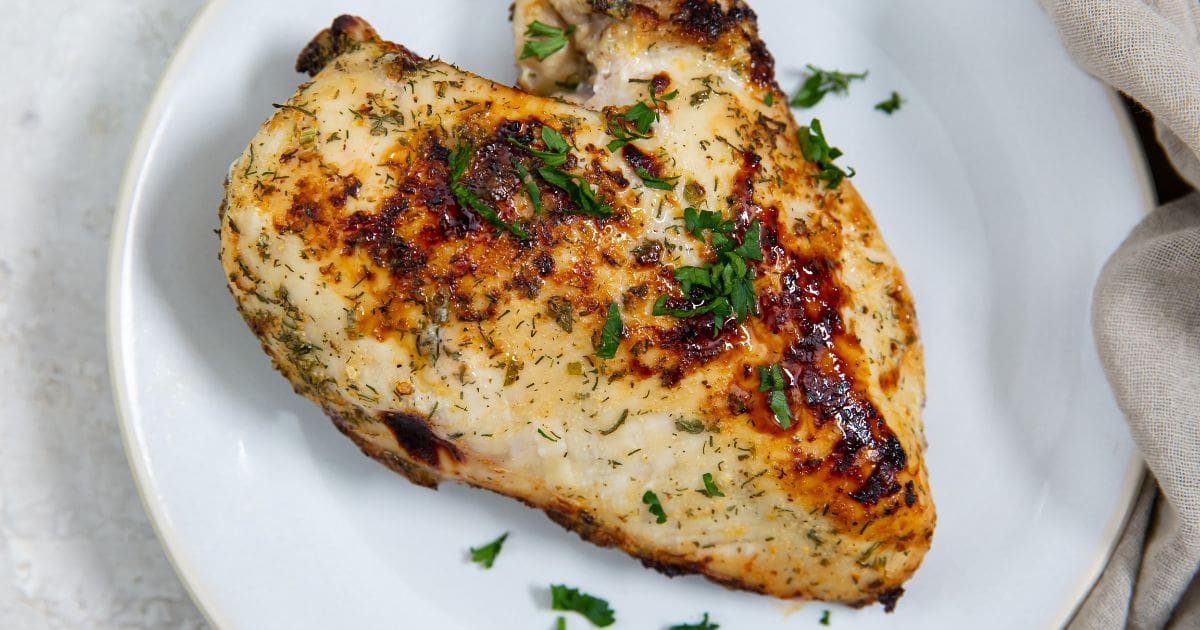 white plate with chicken breast on it parsley in the back green towel next to it