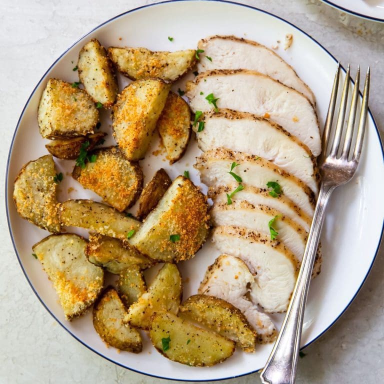 two plates with chicken and potatoes fork on plate parsley in the back