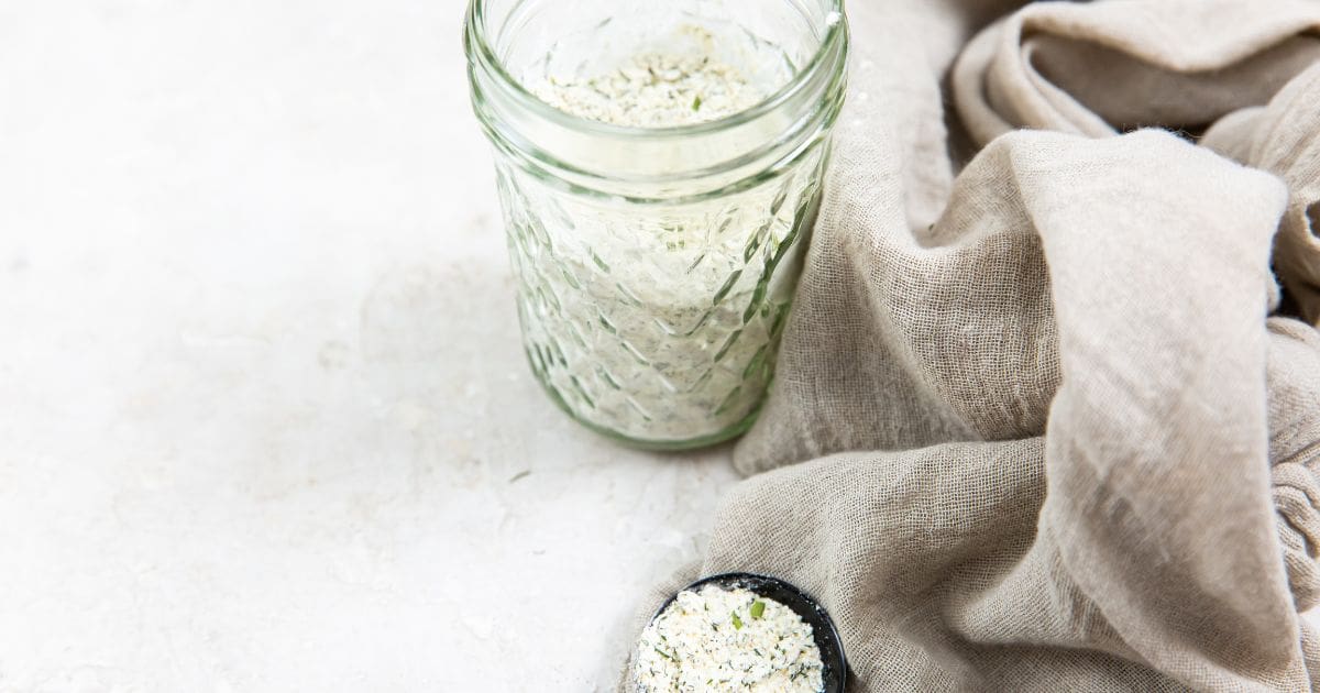 mason jar with ranch seasoning. gray towel next to it and tablespoon with ranch seasoning on top of it.