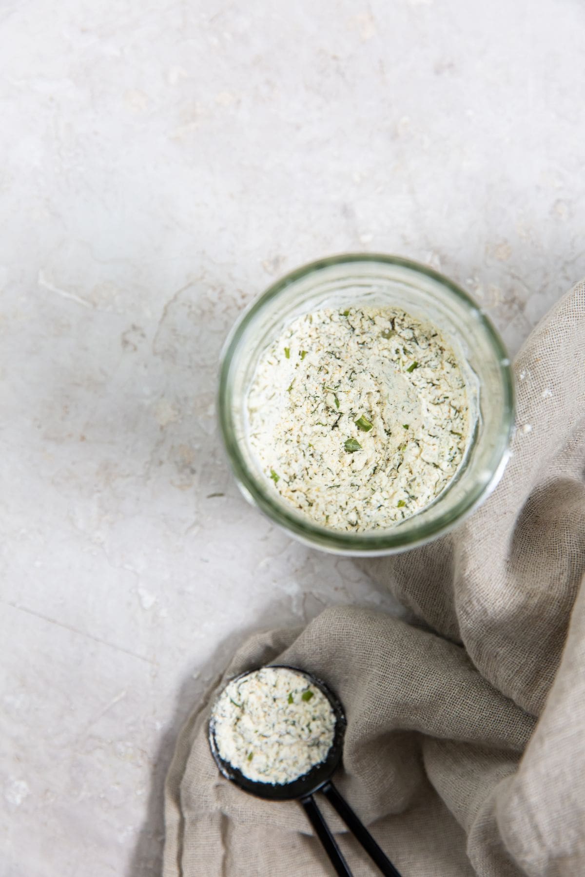 mason jar with ranch seasoning. gray towel next to it and tablespoon with ranch seasoning on top of it.