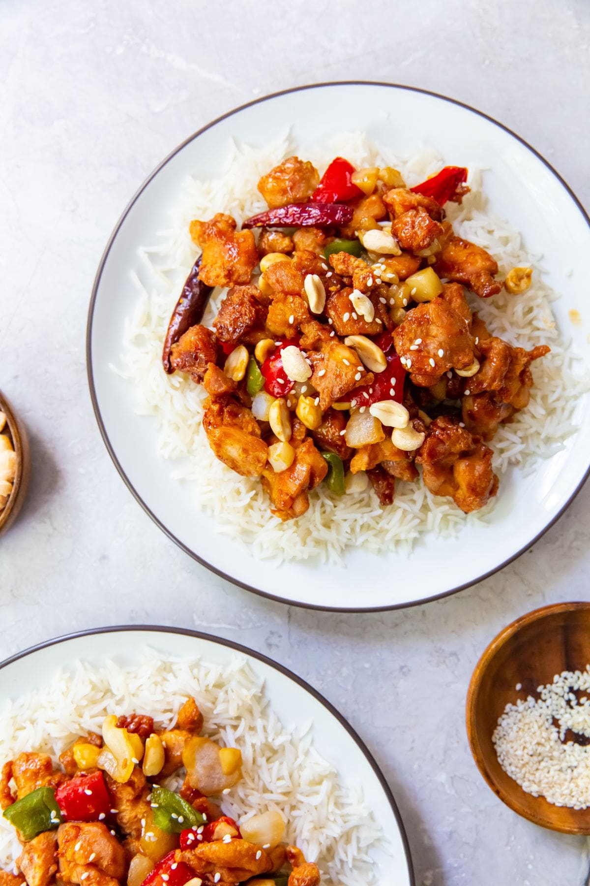 two plate with rice and kung pao chicken on it. bowl of peanuts and sesame seeds next to it