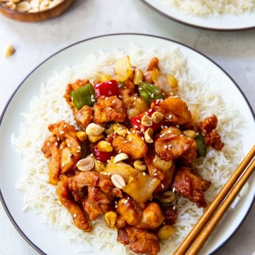 two plate with rice and kung pao chicken on it. bowl of peanuts next to it chopsticks on one plate.