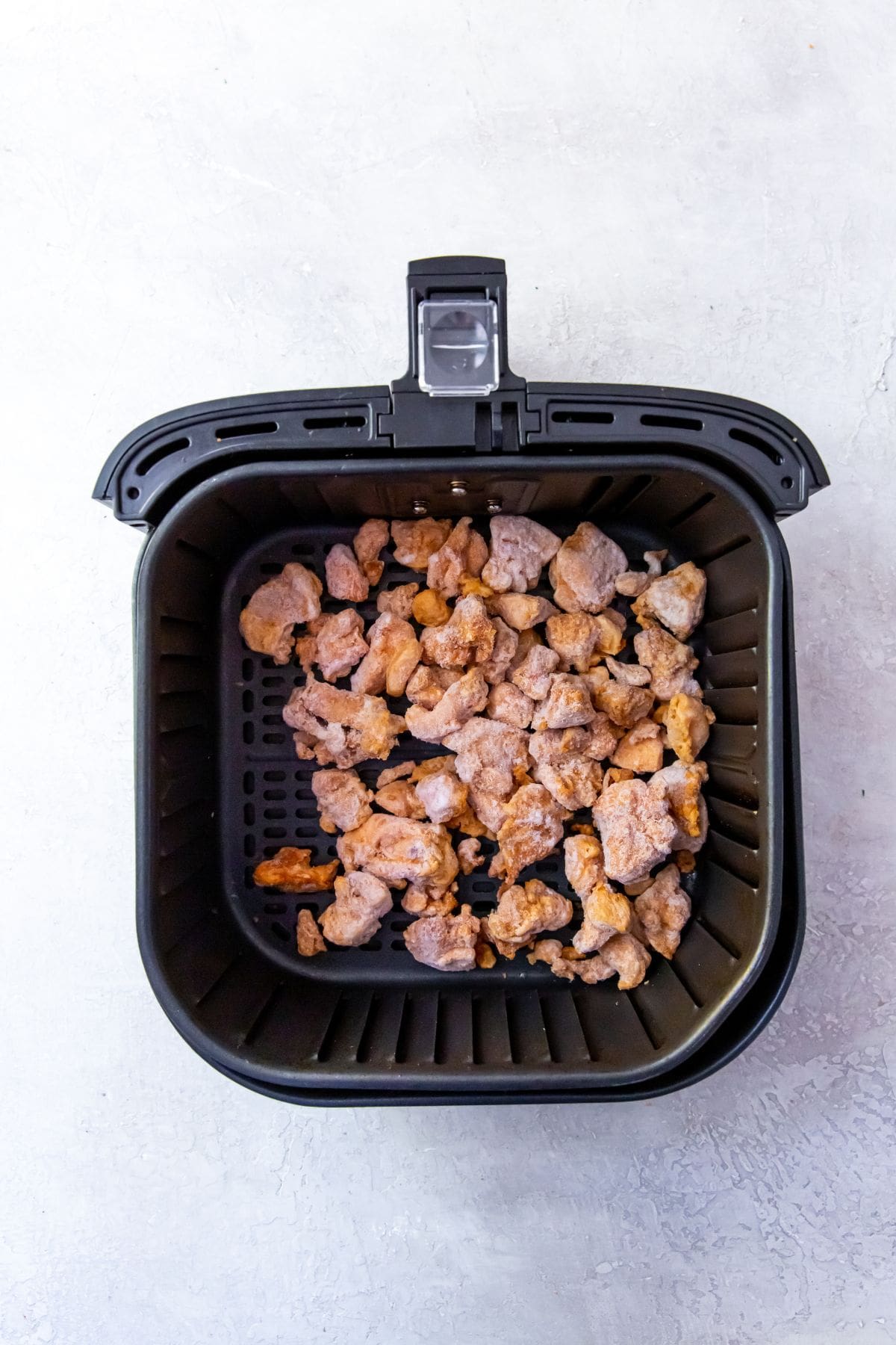 Black air fryer with frozen chicken inside