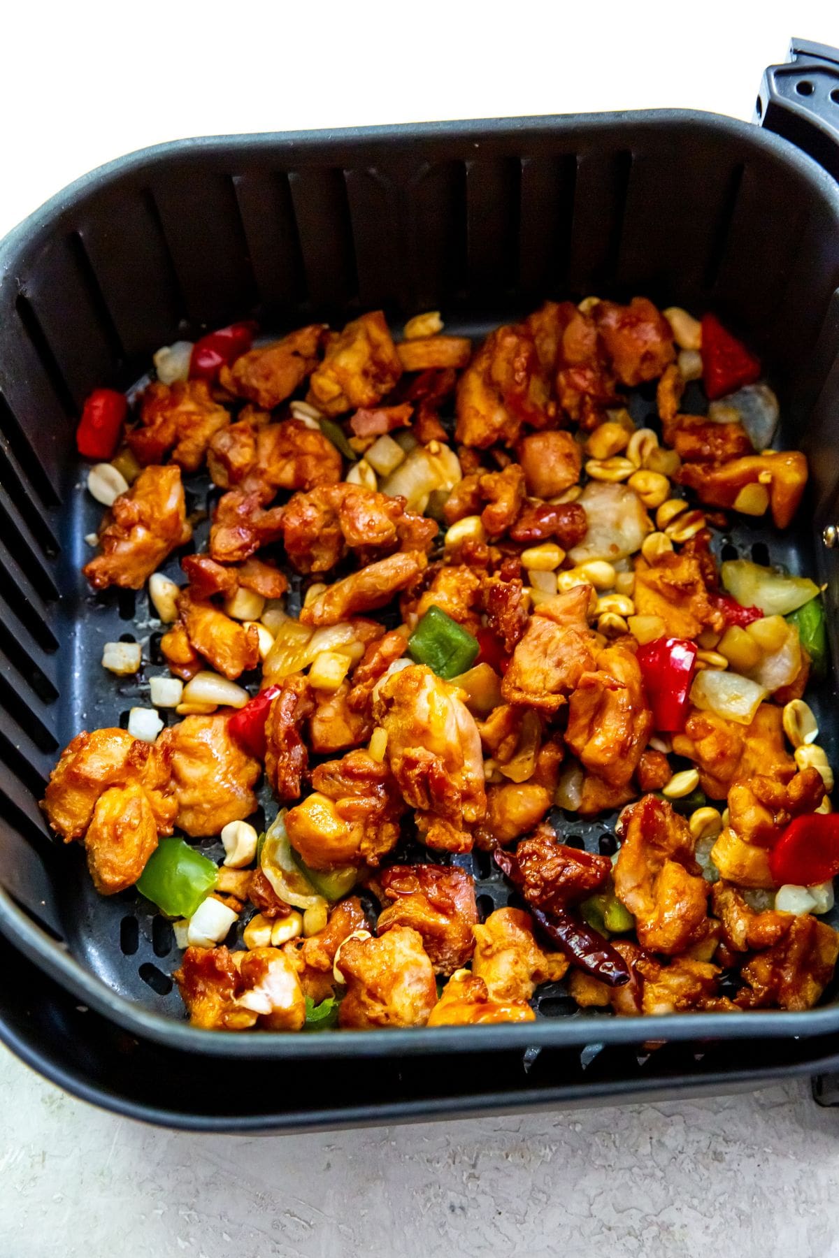 black air fryer with cooked chicken and vegetables inside peanuts topped with it.