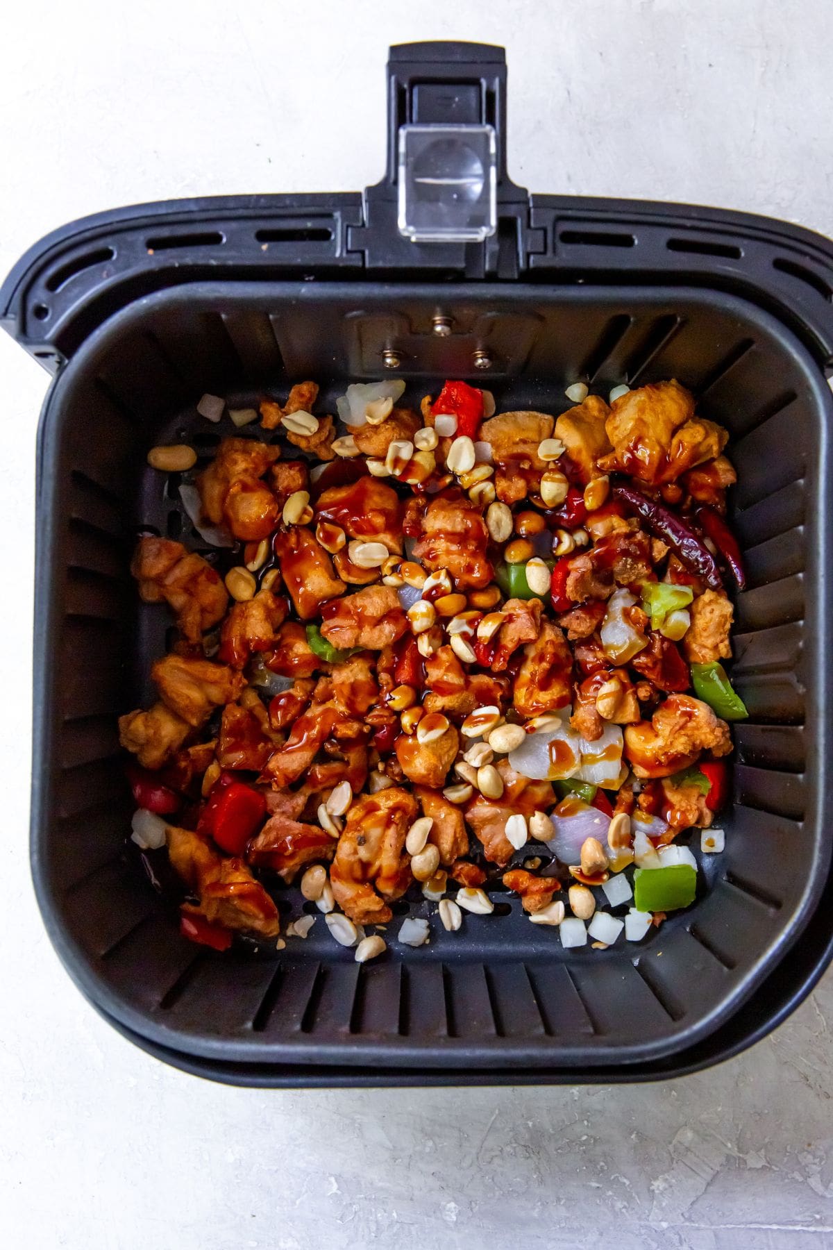 black air fryer with cooked chicken and vegetables inside peanuts topped with it.