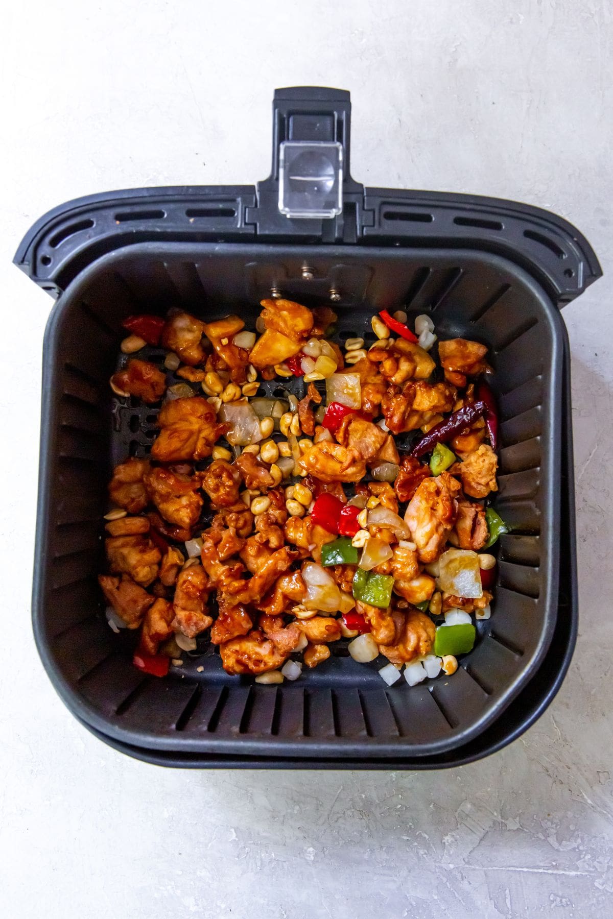 black air fryer with cooked chicken and vegetables inside peanuts topped with it.