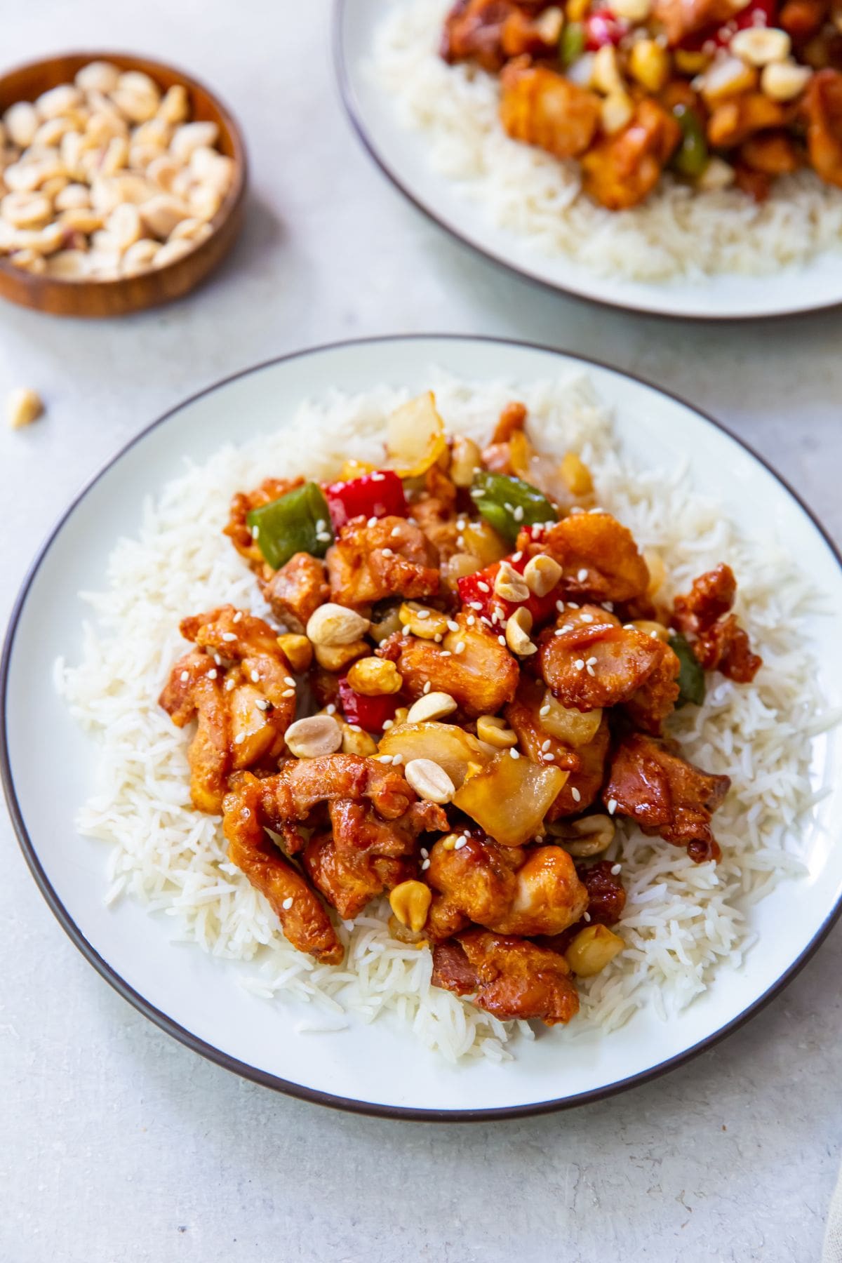 two plate with rice and kung pao chicken on it. bowl of peanuts next to it