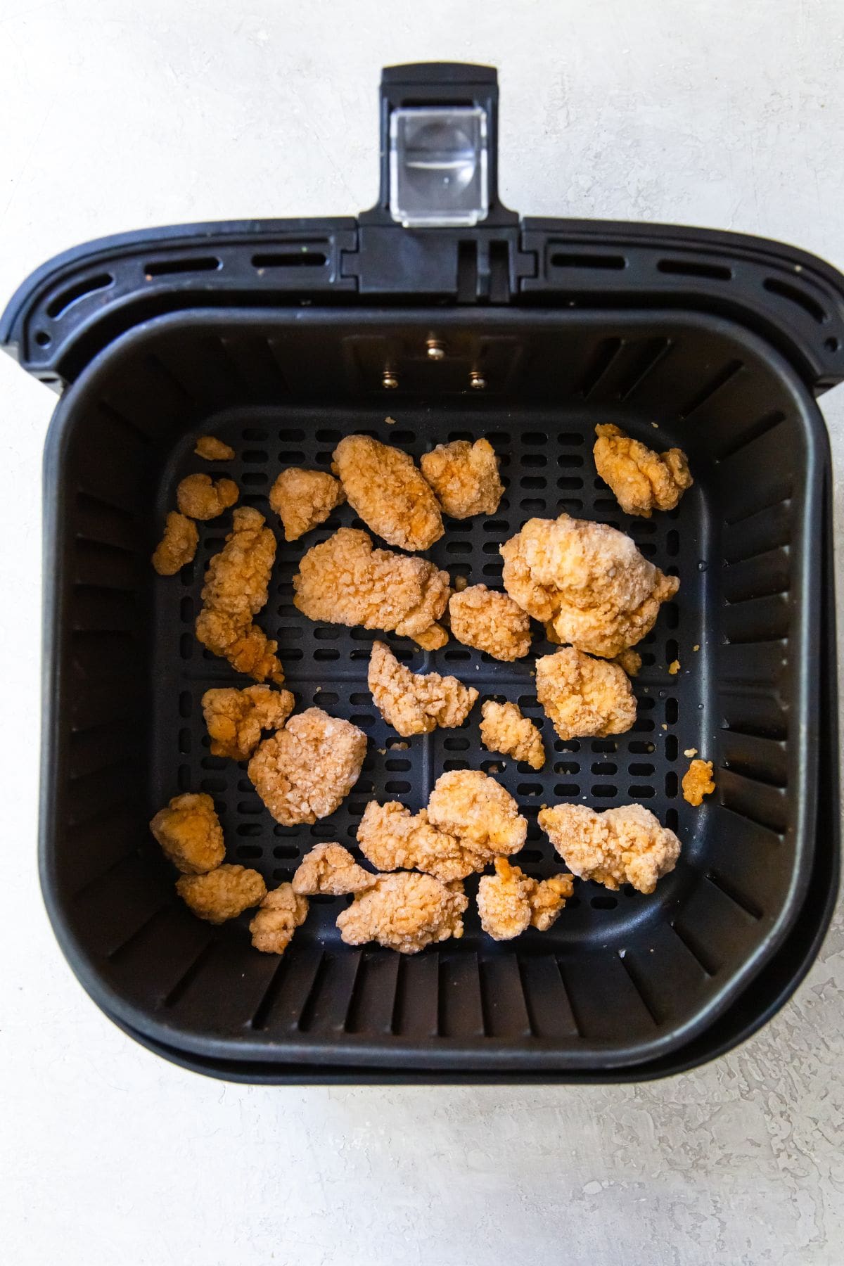 black air fryer with frozen popcorn chicken inside