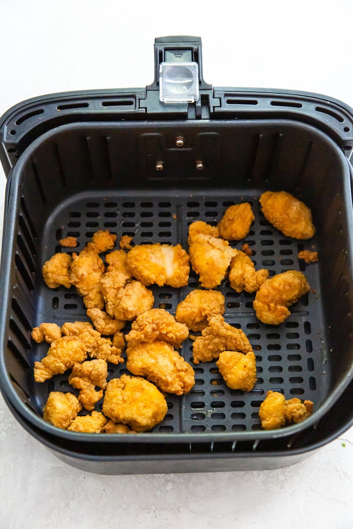 black air fryer with cooked popcorn chicken inside