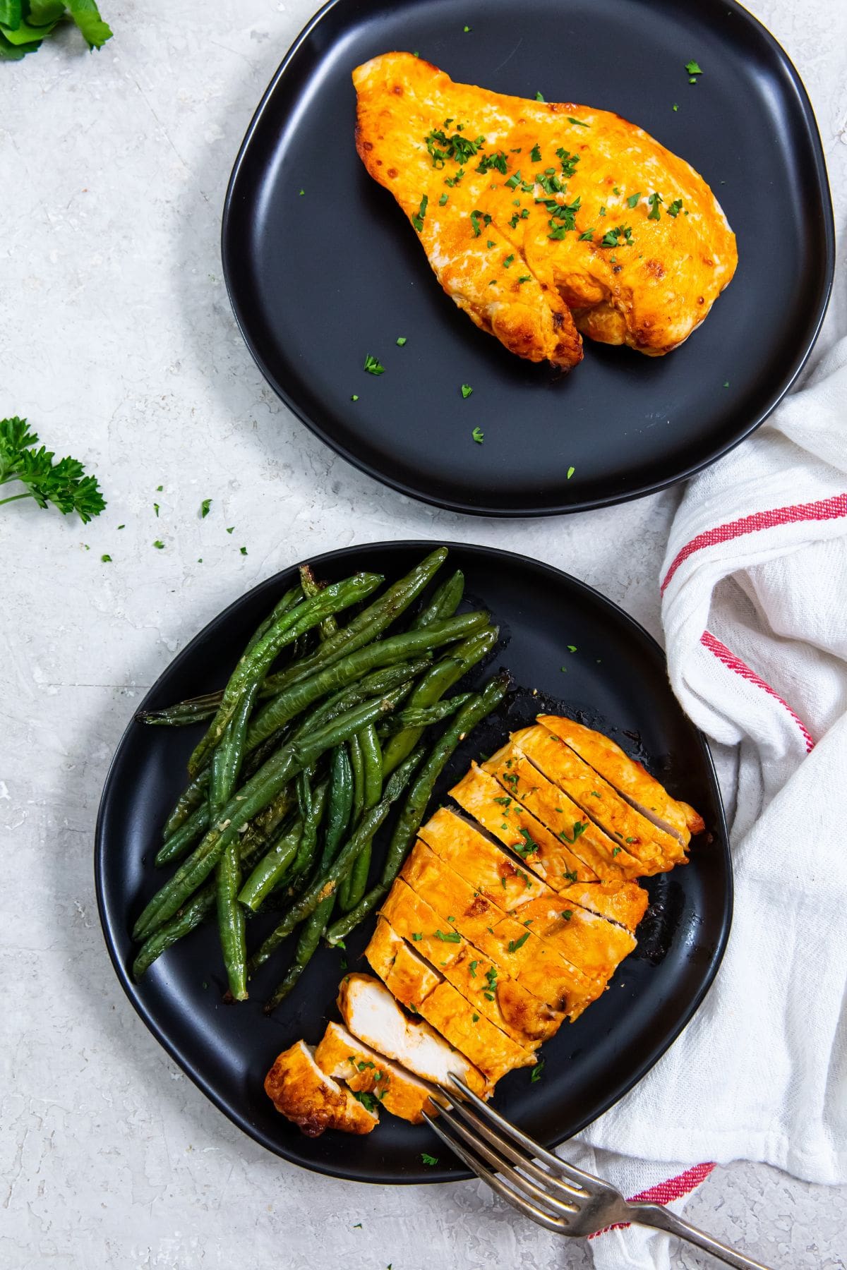 black plate with chicken cut up and green beans another plate with chicken