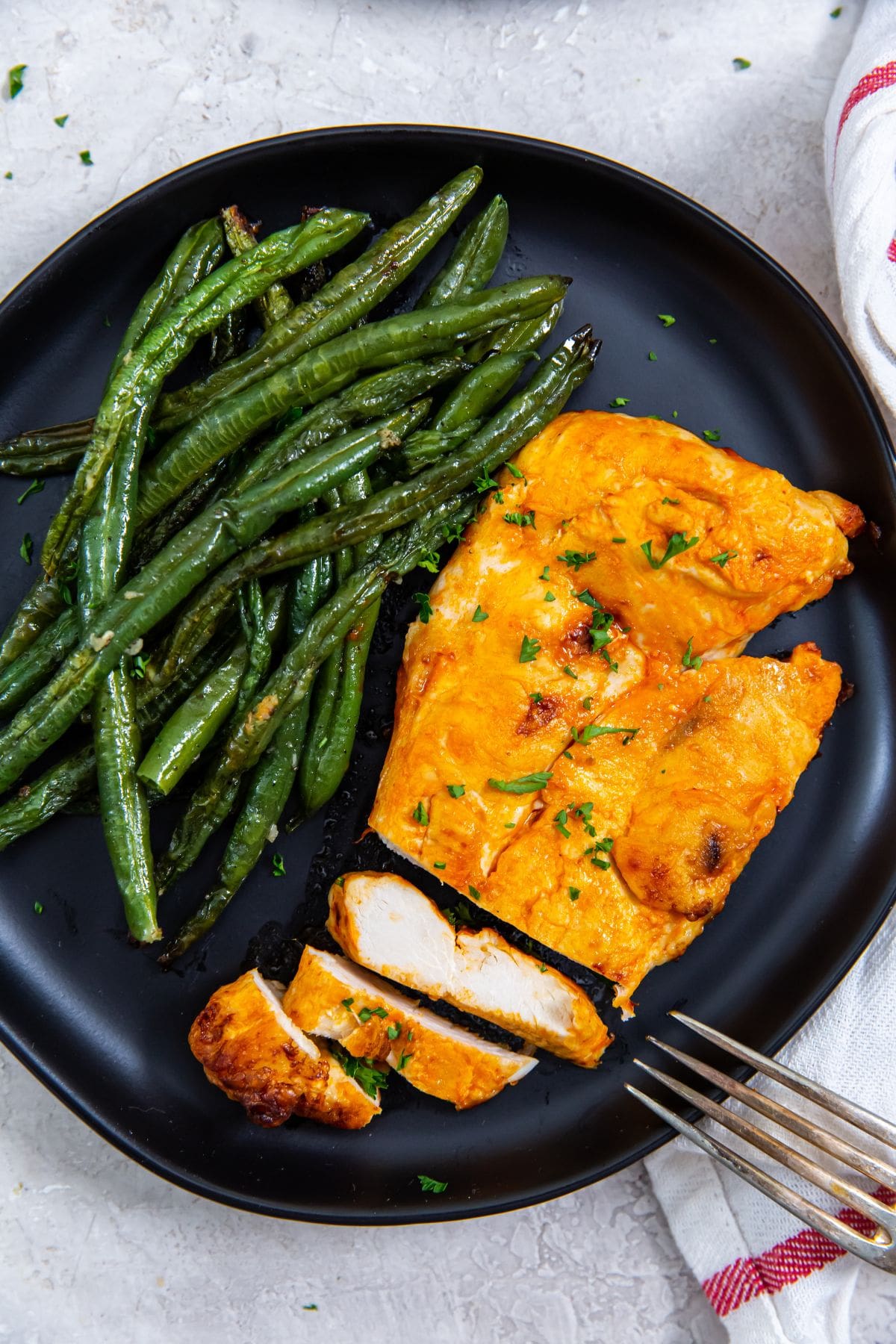 black plate with a chicken cut-up fork on the plate. green beans on the plate