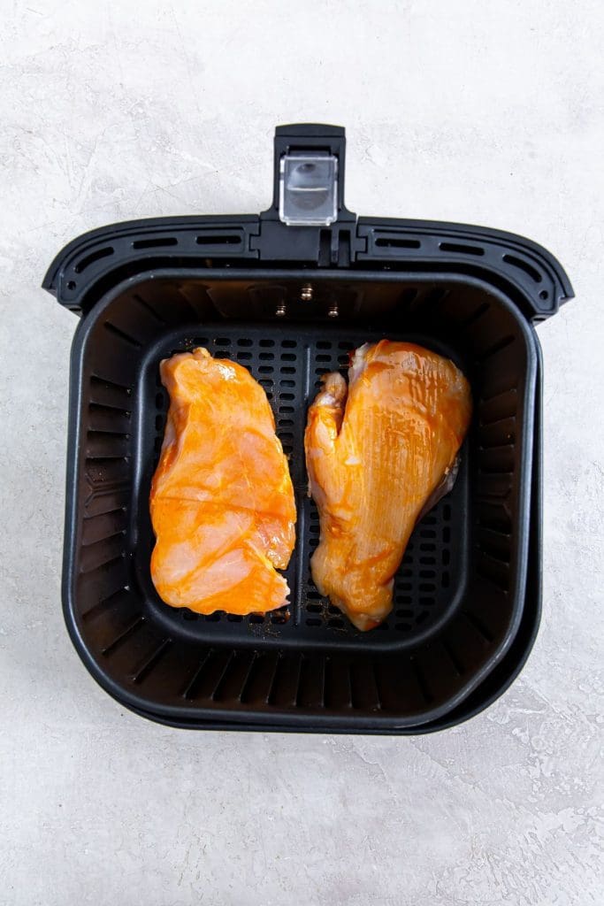 black air fryer with raw chicken inside