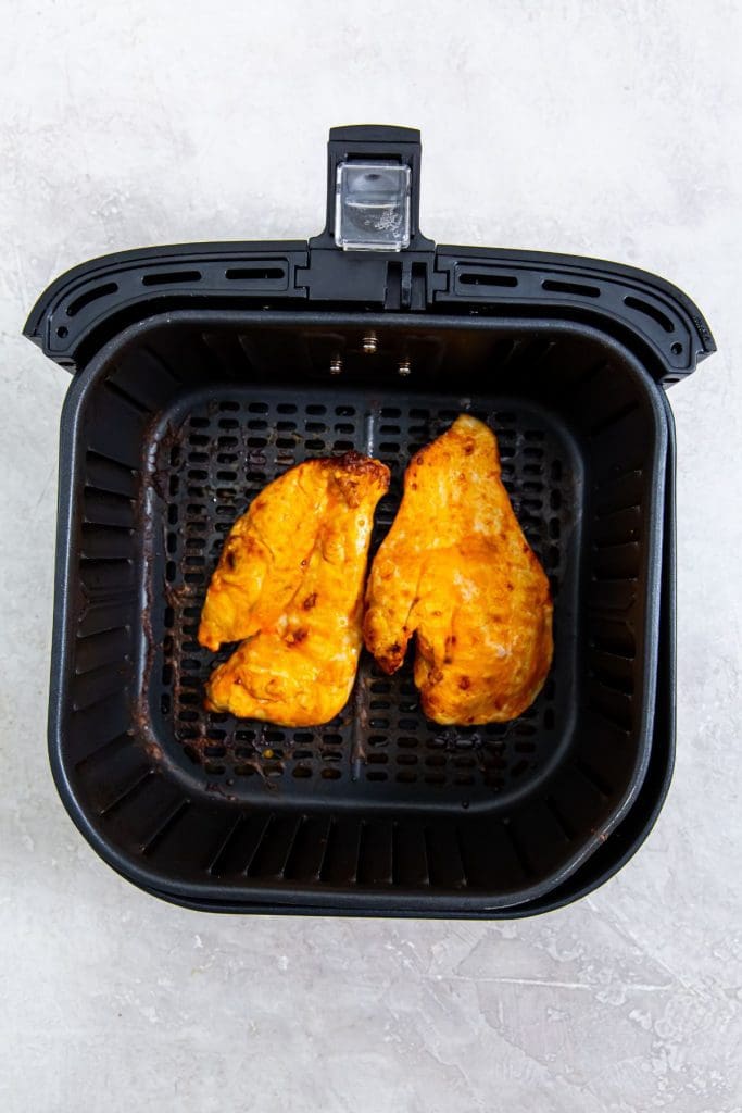 black air fryer with cooked chicken inside