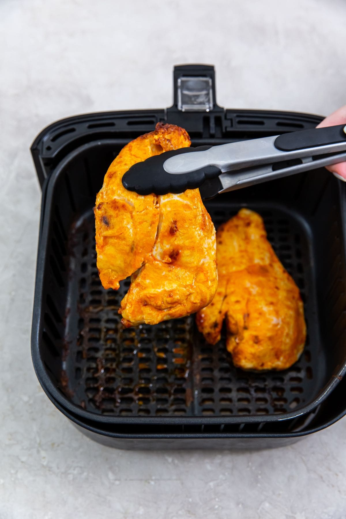 black air fryer with cooked chicken inside. tongs holding one half