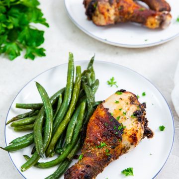 white plate with chicken on it. one plate has green beans on it. parsley in the back.