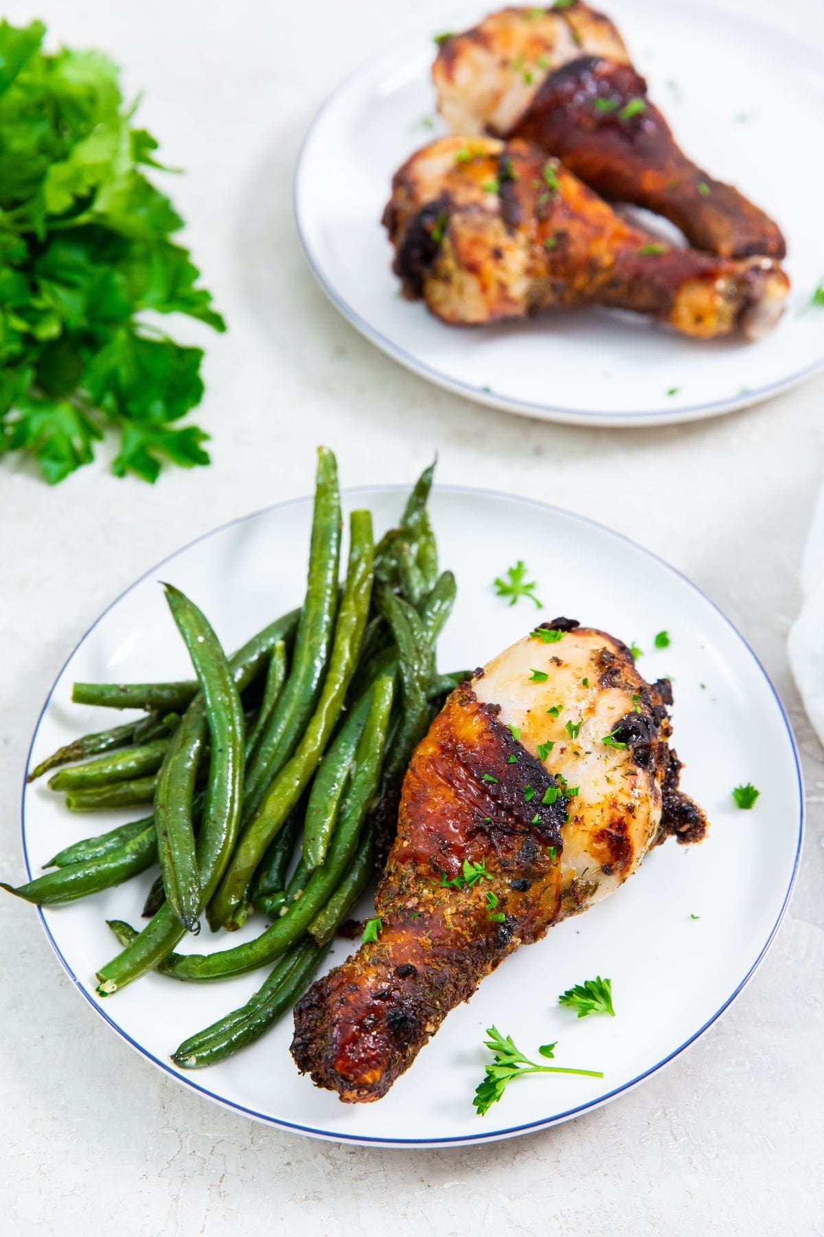 white plate with chicken on it. one plate has green beans on it. parsley in the back.