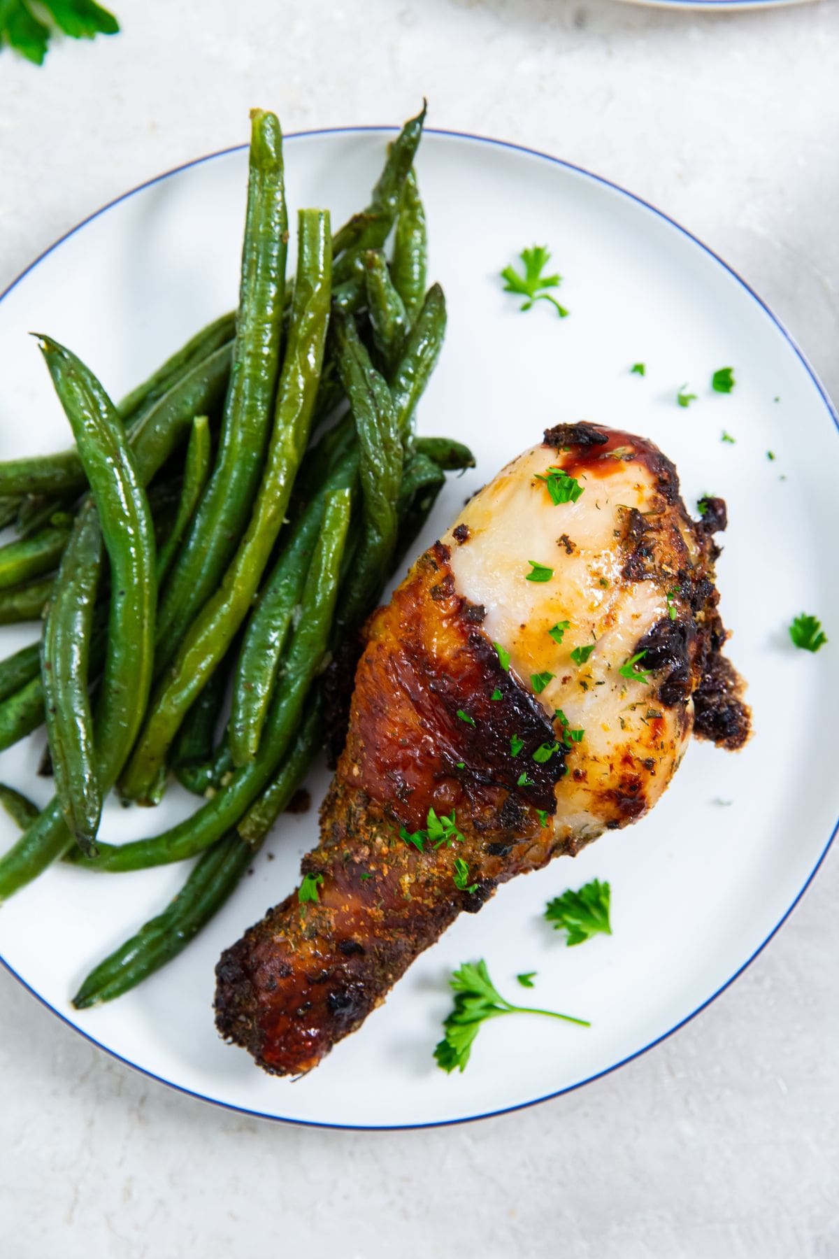 white plate with chicken on it. one plate has green beans on it. parsley in the back.