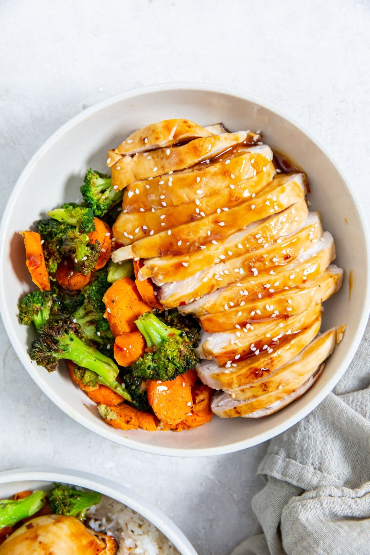 white bowl with chicken veggies and rice inside. gray towel next to it